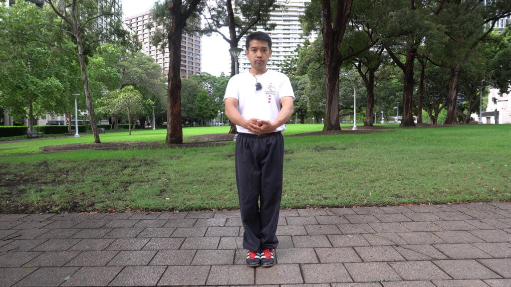 Posição inicial do exercicio 05 do tai chi chuan. Pés juntos com a mãos sobrepostas para frente na altura da barriga.